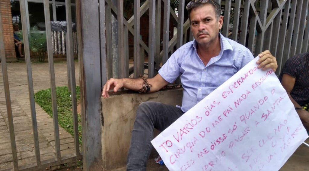 Homem se acorrenta na frente de hospital para cobrar cateterismo no pai internado há 10 dias no AC